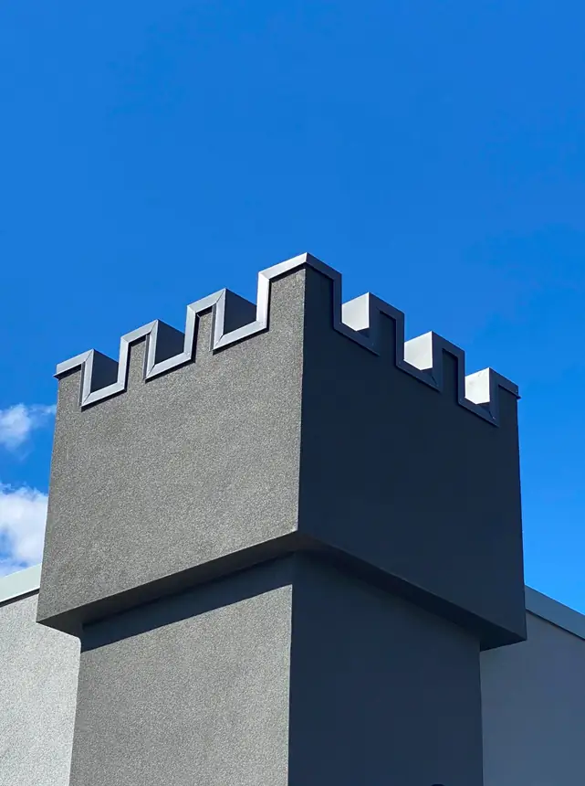 Crenellated tower with fabricated grey metal caps against a blue sky