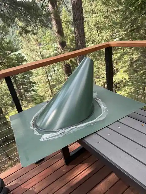 Green flue boot flashing on a deck roof among pines