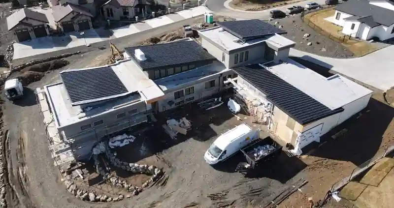 Drone view of new-build homes with dark metal roofs and crew vans on site