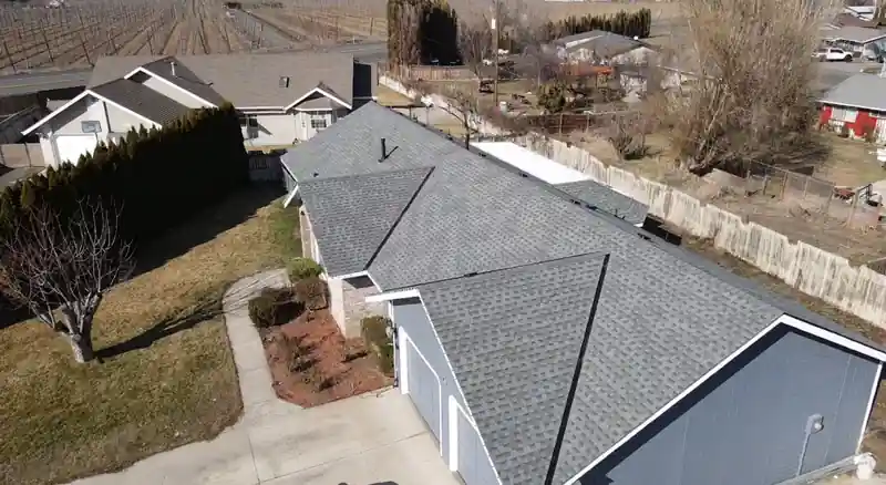 Drone view of a single-storey home with a new grey shingle roof, orchard behind