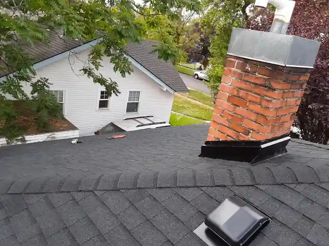Brick chimney with a new metal cap and flashing on a new shingle roof